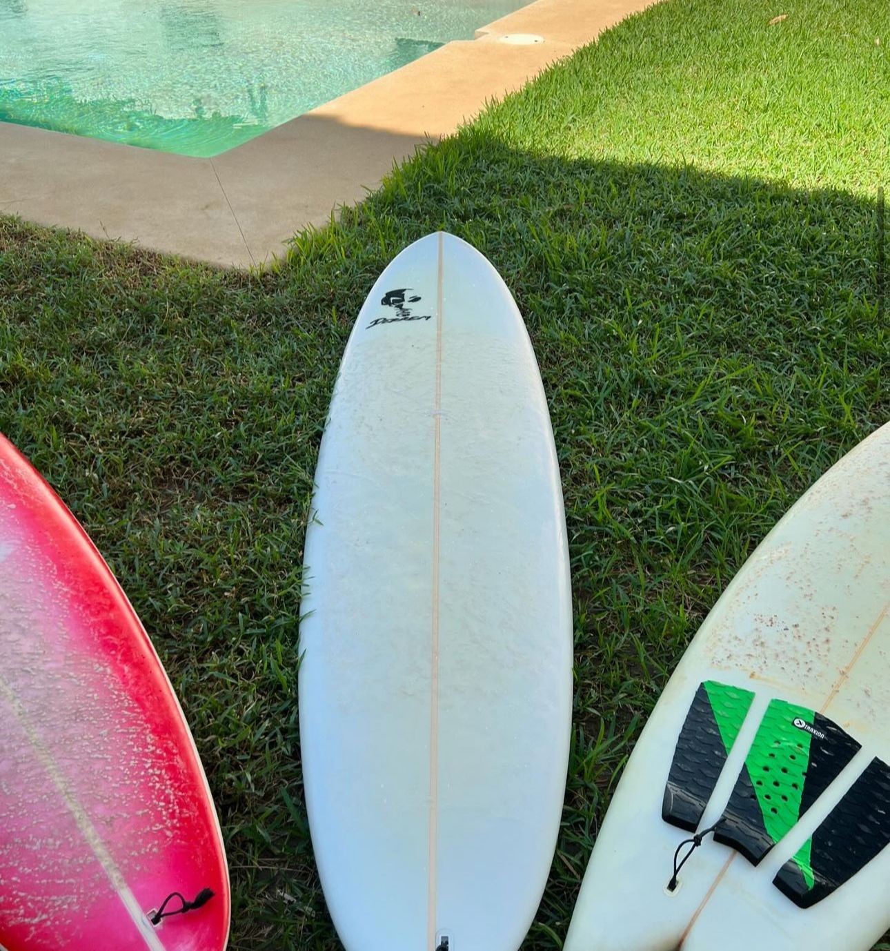 Three surfboards resting on grass near a swimming pool edge.