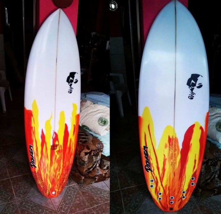 Surfboard with red and yellow flame design leaning against a wall.