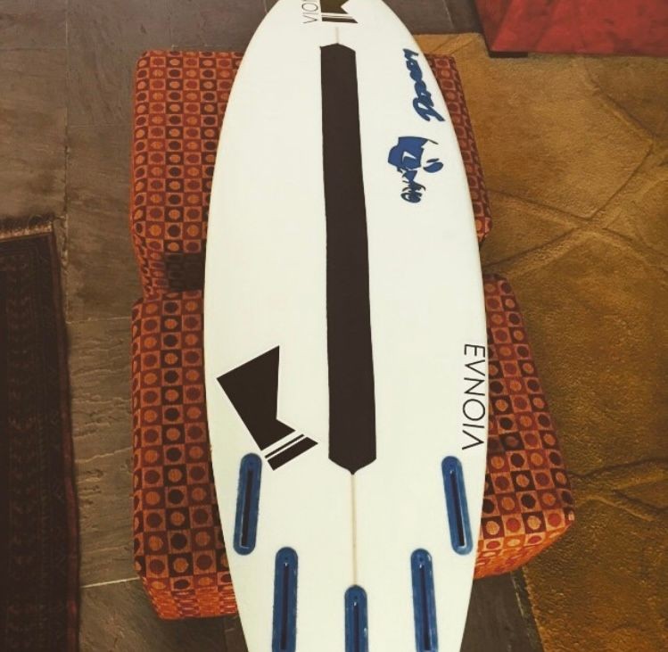 Surfboard with black and blue designs placed on an orange patterned couch.