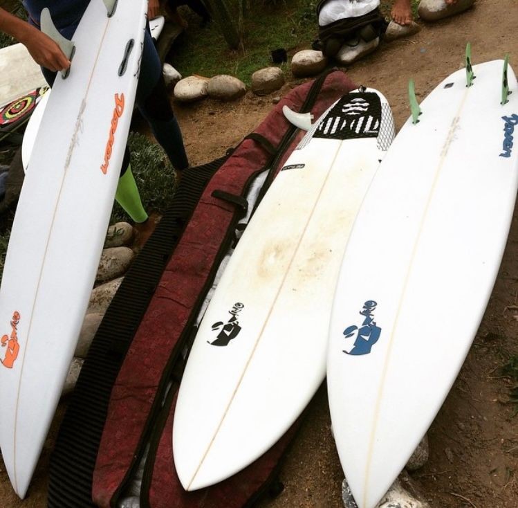 Three surfboards on the ground with colorful decals, surrounded by rocks.